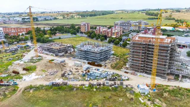 Il lotto con le due gru: a destra l'Edificio A, al centro il B, a sinistra le strutture del C — fotografia di cantiere, giugno 2026