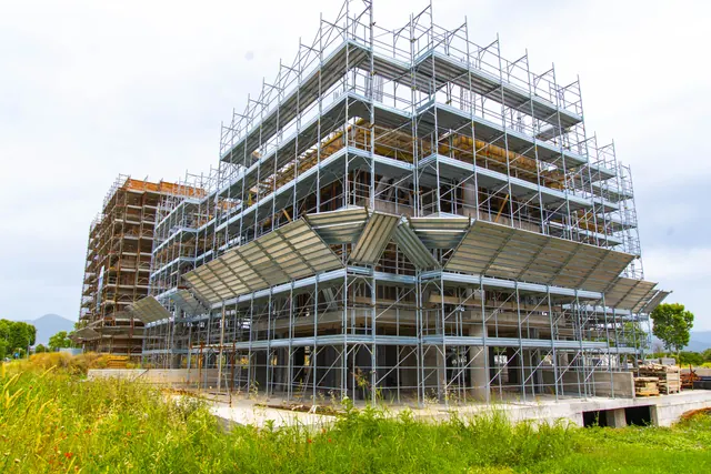 Edificio B in costruzione; dietro, l'Edificio A — fotografia di cantiere, giugno 2026