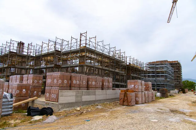 Materiali a piè d'opera: i blocchi per le murature accanto alle strutture in elevazione — fotografia di cantiere, giugno 2026